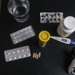 Top view of various medications, tablets, and medical devices on a table with a glass of water.