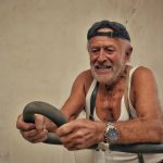 Elderly man smiling while working out on exercise equipment indoors.